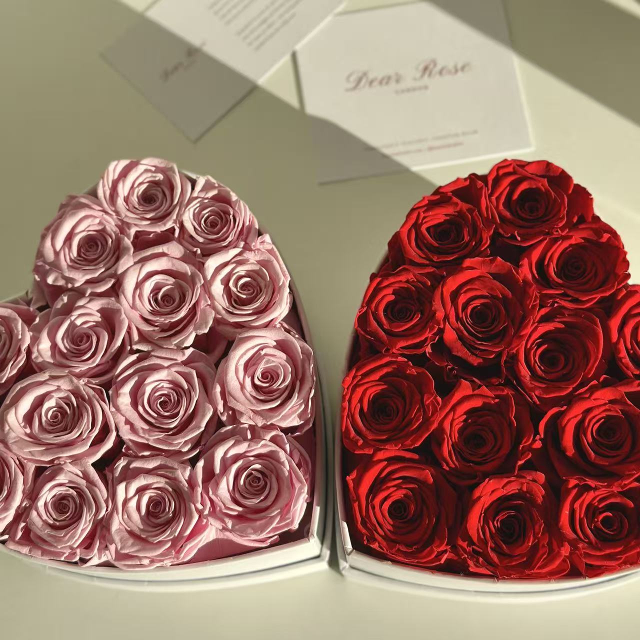 Heart-shaped boxes filled with pink and red roses on a light background